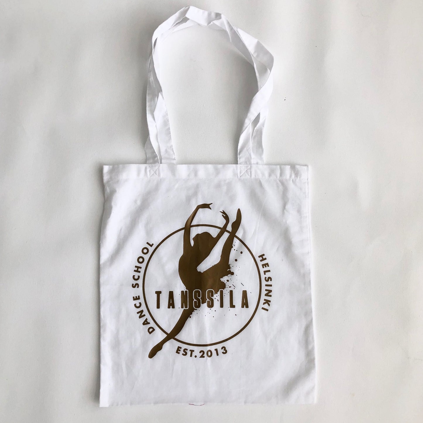 Tanssila, valkoinen kassi kultaisella logolla